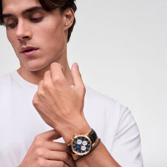 Daniel Wellington Iconic Chronograph Sheffield Arctic Panda Rose Gold watch with an arctic blue dial and black leather strap, worn by a man adjusting it on his wrist.