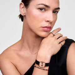 A model wears the Daniel Wellington Margot Sheffield watch, featuring a rose gold case, sunray dial, and black leather strap, styled elegantly with matching rose gold jewelry.