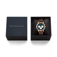 Daniel Wellington Iconic Chronograph St Mawes watch with a gold case, arctic blue panda dial, and brown leather strap, presented in its black gift box.